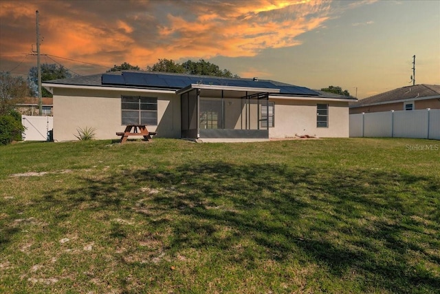 back house at dusk with solar panels, a yard, and a sunroom