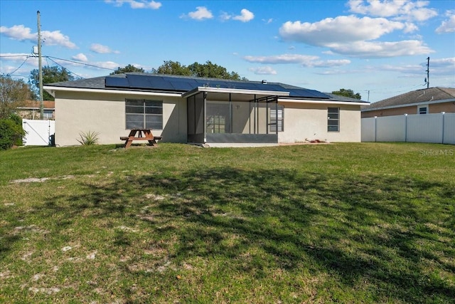 back of house featuring a sunroom, a yard, and solar panels