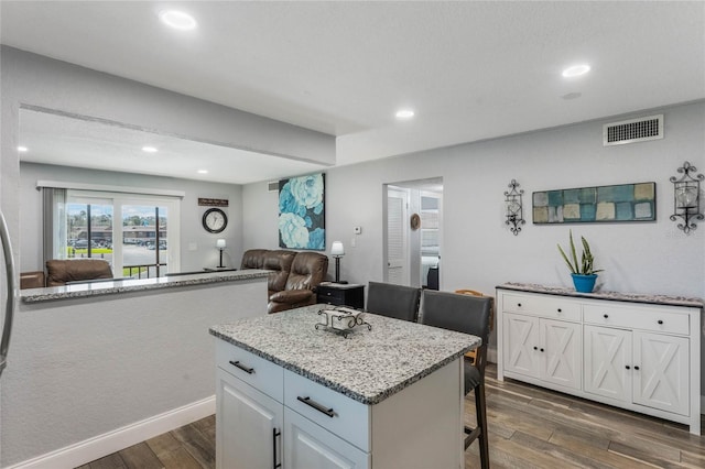 kitchen with a breakfast bar area, white cabinetry, a center island, and dark hardwood / wood-style floors