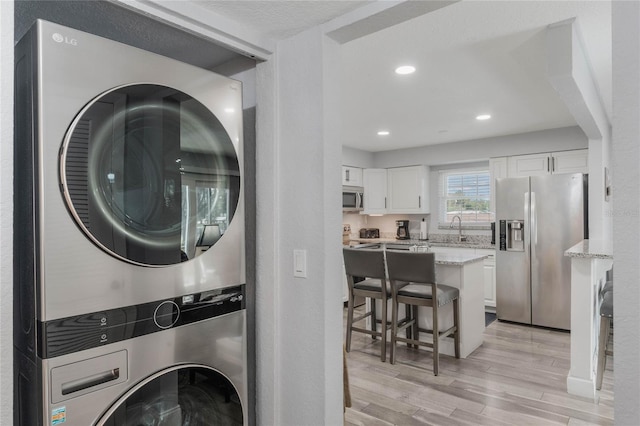 washroom featuring sink, light hardwood / wood-style floors, and stacked washer / drying machine