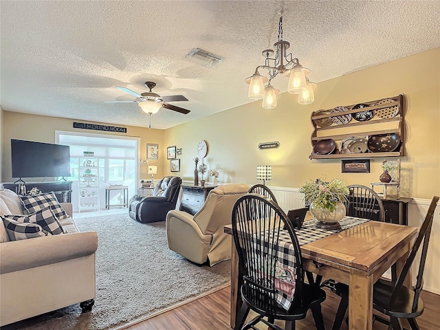 dining room with ceiling fan with notable chandelier, dark wood-type flooring, and a textured ceiling