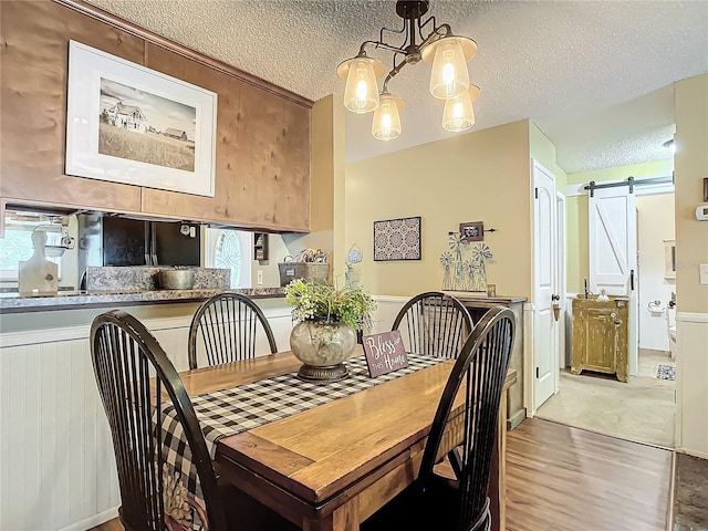 dining area with a textured ceiling, a barn door, and hardwood / wood-style flooring