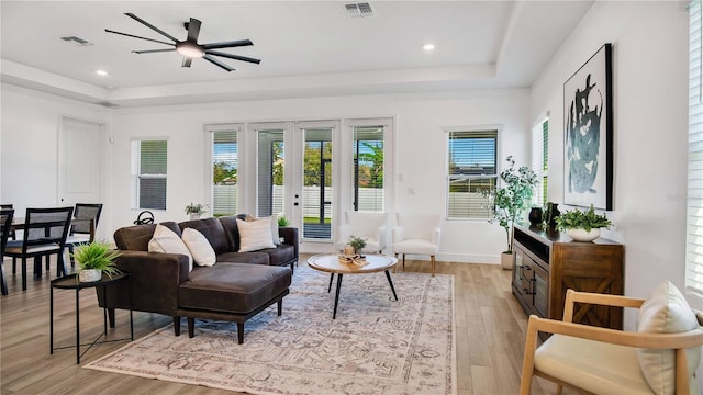 living room featuring ceiling fan, light hardwood / wood-style floors, french doors, and a tray ceiling