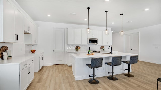 kitchen featuring pendant lighting, light hardwood / wood-style floors, white cabinetry, and a kitchen island with sink