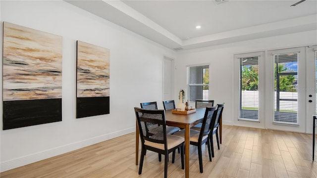 dining area with light wood-type flooring and a tray ceiling