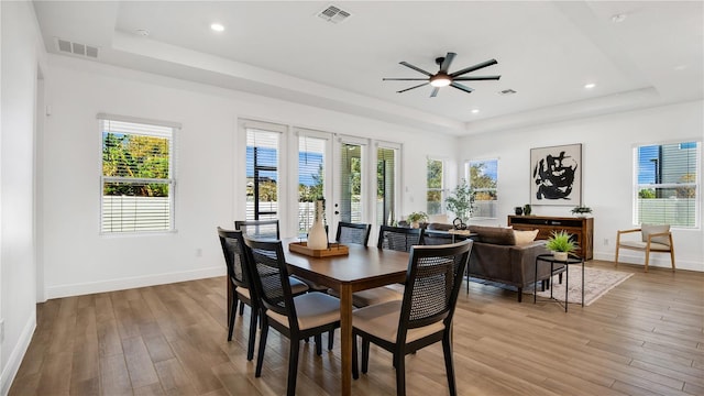 dining space featuring light wood-type flooring, a raised ceiling, plenty of natural light, and ceiling fan