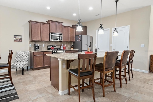 kitchen featuring light stone countertops, hanging light fixtures, stainless steel appliances, a kitchen bar, and a kitchen island with sink