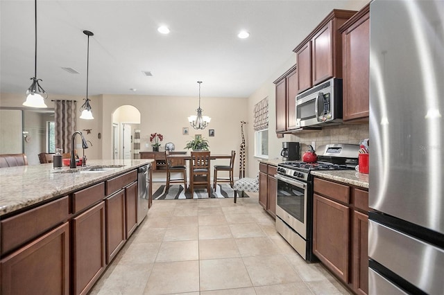 kitchen featuring light stone counters, sink, pendant lighting, and appliances with stainless steel finishes