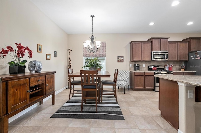 kitchen with decorative backsplash, appliances with stainless steel finishes, dark brown cabinets, light stone counters, and a chandelier