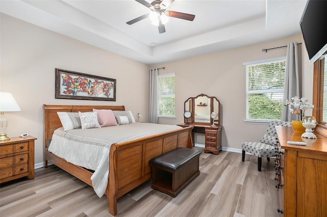 bedroom featuring ceiling fan, a tray ceiling, and light hardwood / wood-style flooring