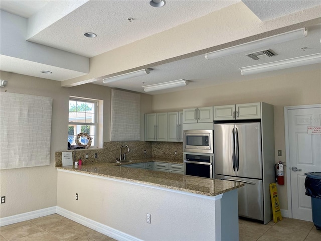 kitchen with light stone countertops, backsplash, kitchen peninsula, light tile patterned floors, and appliances with stainless steel finishes