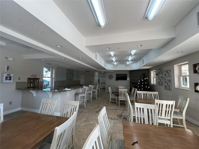 tiled dining area featuring plenty of natural light, a textured ceiling, and a tray ceiling