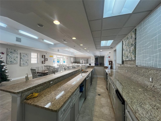 kitchen with a large island, a drop ceiling, dark stone counters, decorative backsplash, and a breakfast bar