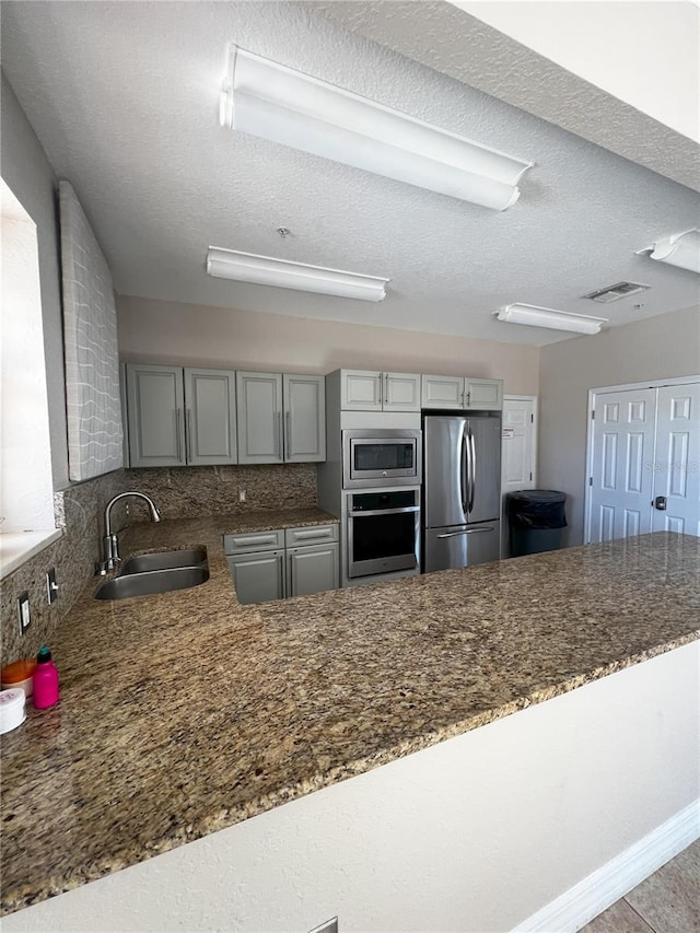 kitchen featuring gray cabinetry, sink, a textured ceiling, kitchen peninsula, and stainless steel appliances