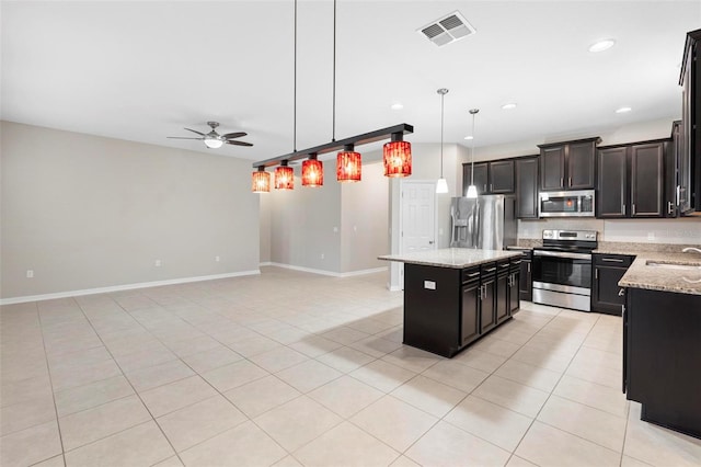 kitchen with ceiling fan, stainless steel appliances, light stone counters, decorative light fixtures, and a kitchen island