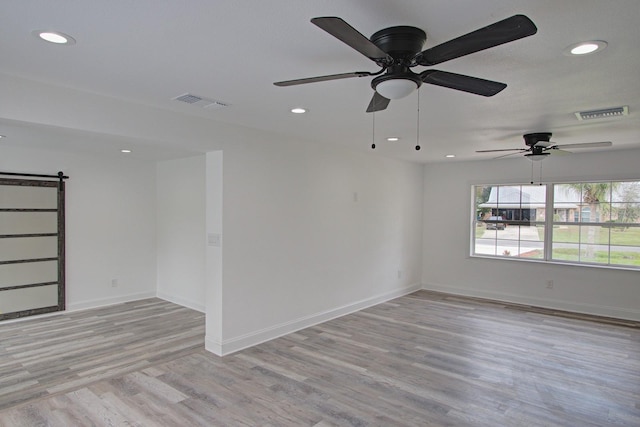 empty room with a barn door, ceiling fan, and light wood-type flooring