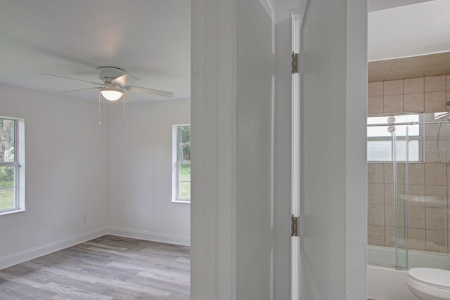 bathroom with hardwood / wood-style floors, toilet, a wealth of natural light, and bath / shower combo with glass door