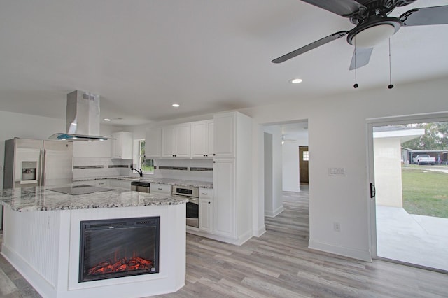 kitchen featuring light stone counters, light hardwood / wood-style flooring, island exhaust hood, white cabinets, and appliances with stainless steel finishes