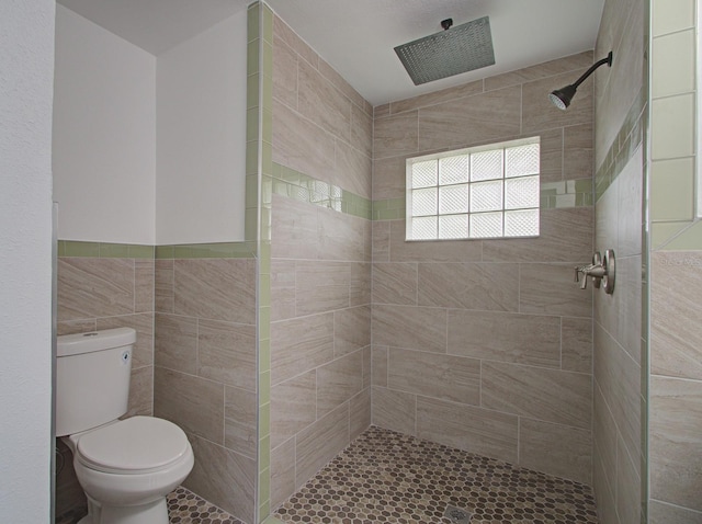 bathroom with a tile shower, toilet, and tile walls