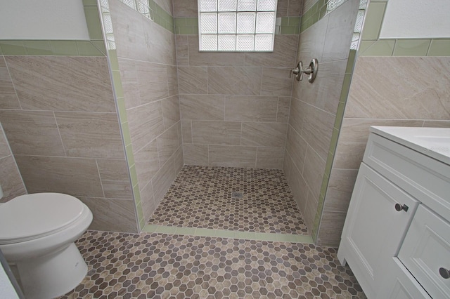 bathroom featuring vanity, tile patterned floors, toilet, tile walls, and a tile shower