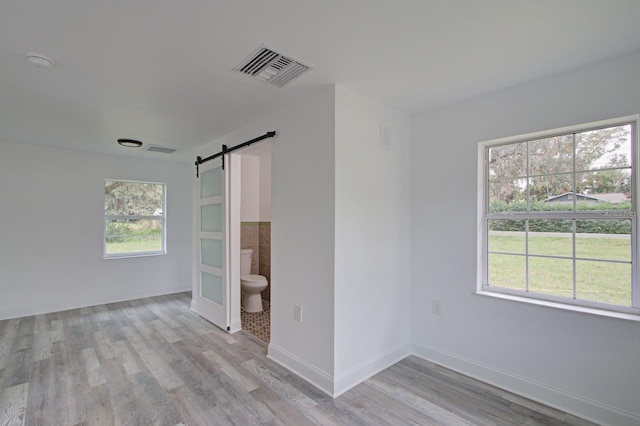 spare room with a barn door, light wood-type flooring, and a healthy amount of sunlight