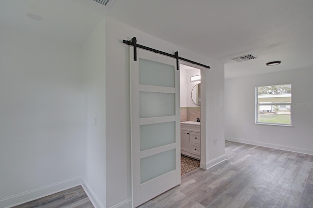 unfurnished bedroom featuring light wood-type flooring, connected bathroom, and a barn door