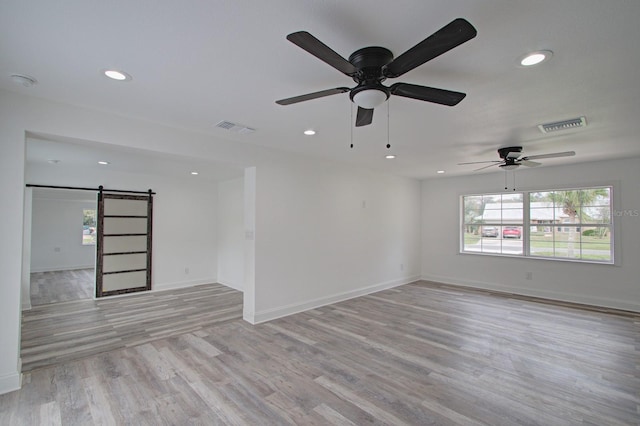 empty room featuring ceiling fan, a barn door, and light hardwood / wood-style floors