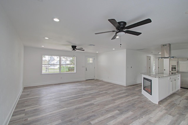 kitchen with white cabinetry, ceiling fan, light stone counters, island exhaust hood, and light wood-type flooring