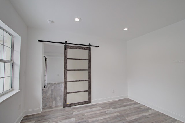 empty room with a barn door, light hardwood / wood-style flooring, and a wealth of natural light