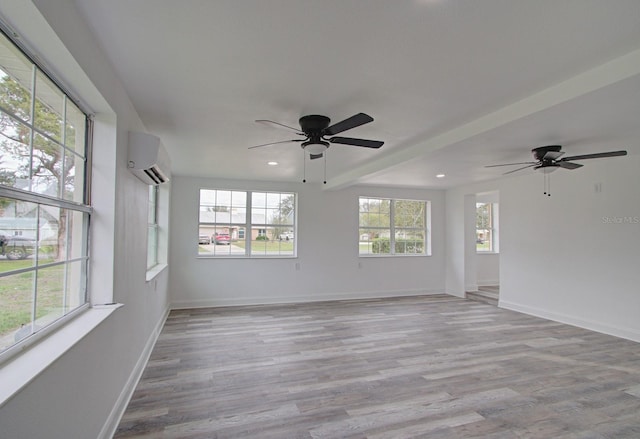 empty room featuring ceiling fan, a wall unit AC, a wealth of natural light, and light hardwood / wood-style flooring