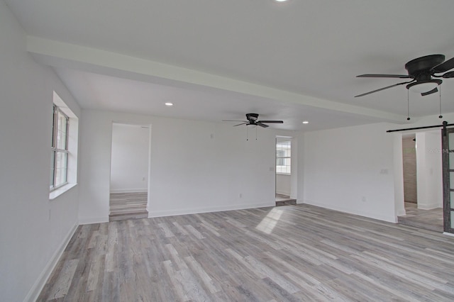 spare room with ceiling fan, a barn door, and light wood-type flooring