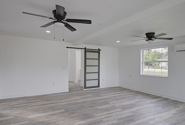 empty room featuring ceiling fan, a barn door, light wood-type flooring, a wall mounted AC, and beam ceiling