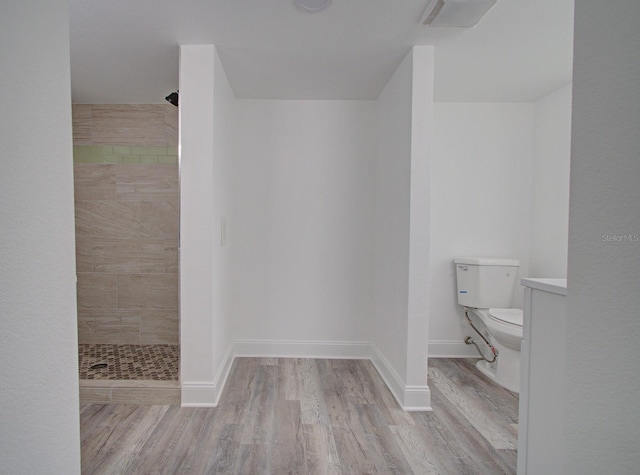 bathroom featuring tiled shower, hardwood / wood-style floors, and toilet