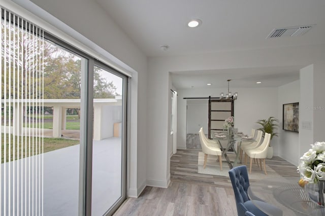 interior space with light wood-type flooring, an inviting chandelier, and a barn door