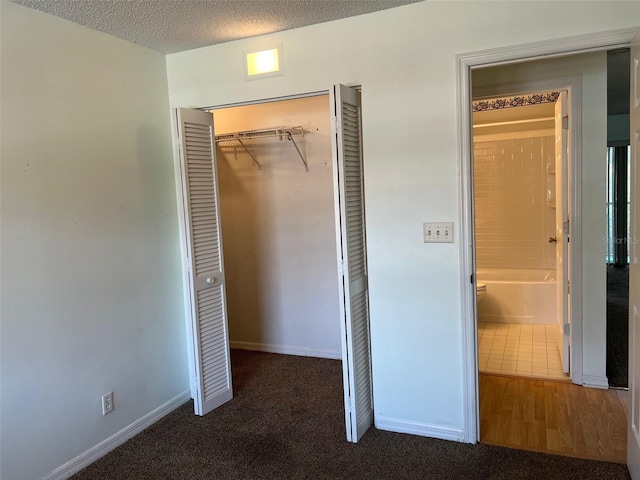 unfurnished bedroom with a textured ceiling, dark carpet, and a closet