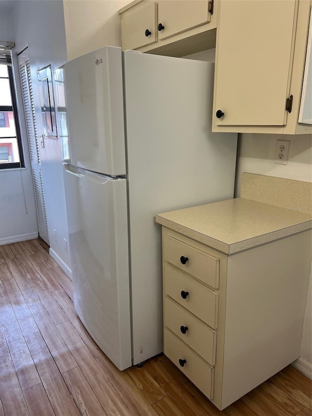 kitchen with white cabinets, white fridge, and light hardwood / wood-style flooring