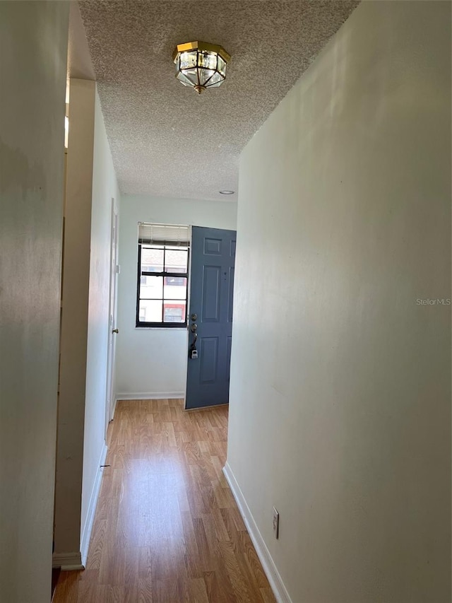 hallway with light wood-type flooring and a textured ceiling