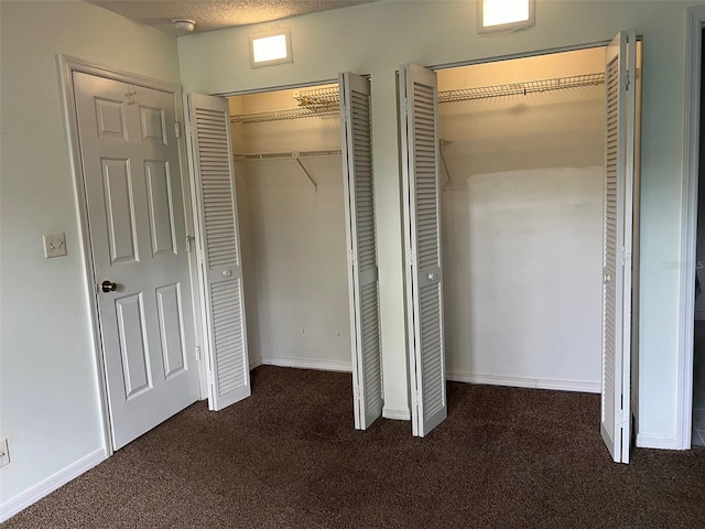 unfurnished bedroom with a textured ceiling, dark carpet, and two closets