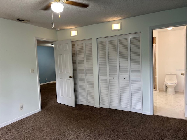 unfurnished bedroom with dark colored carpet, ceiling fan, a textured ceiling, and two closets