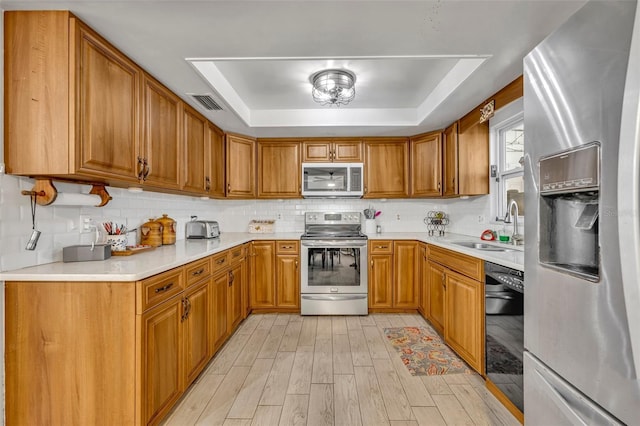 kitchen featuring appliances with stainless steel finishes, a tray ceiling, sink, and backsplash