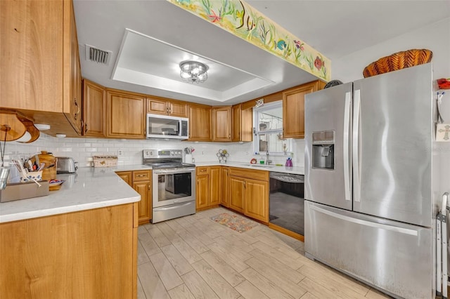 kitchen with sink, appliances with stainless steel finishes, light stone counters, decorative backsplash, and a raised ceiling