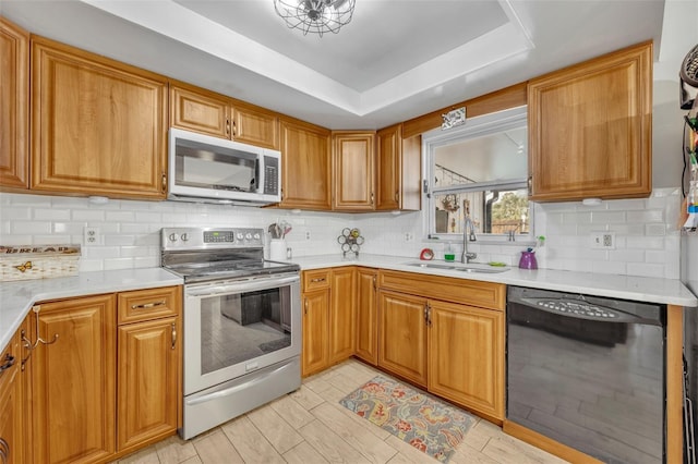 kitchen with tasteful backsplash, appliances with stainless steel finishes, sink, and a tray ceiling