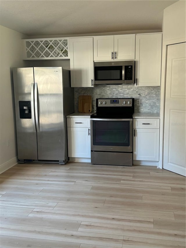 kitchen with tasteful backsplash, white cabinetry, stainless steel appliances, and light wood-type flooring