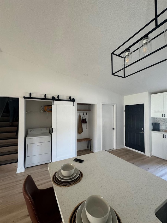 kitchen with white cabinetry, a barn door, vaulted ceiling, washer / dryer, and light wood-type flooring