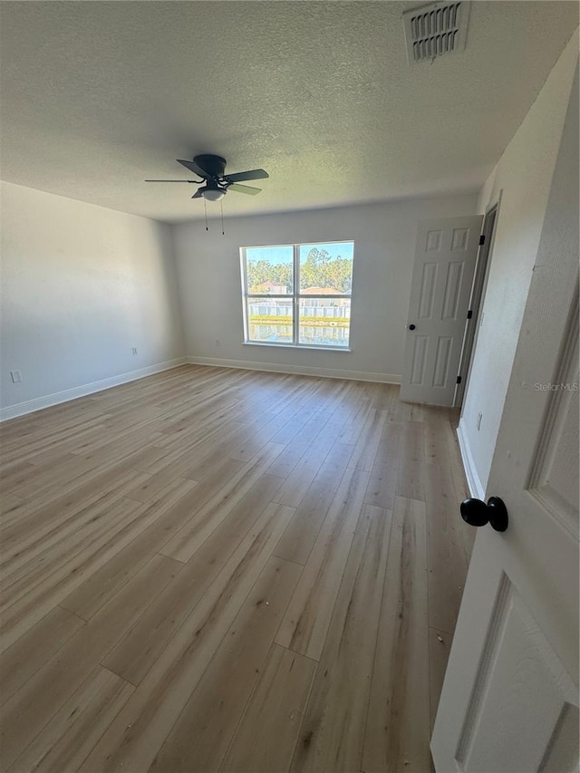 empty room with ceiling fan, light wood-type flooring, and a textured ceiling