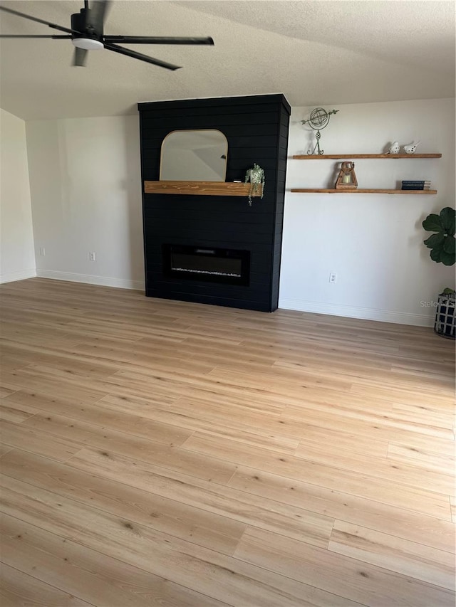 empty room with ceiling fan, a fireplace, a textured ceiling, and light wood-type flooring