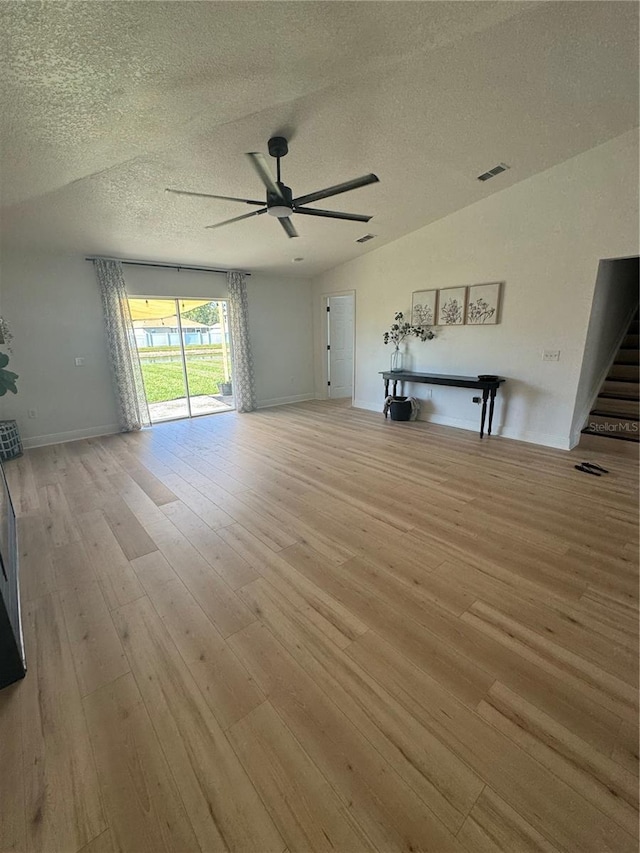 unfurnished living room featuring lofted ceiling, ceiling fan, light hardwood / wood-style floors, and a textured ceiling