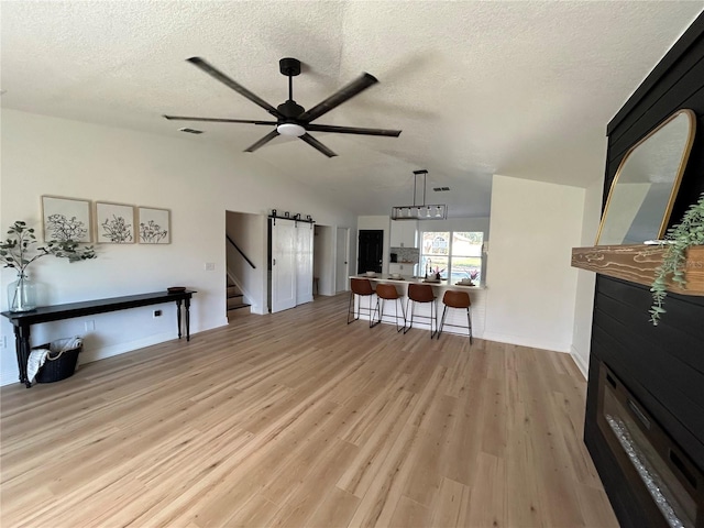 living room with vaulted ceiling, ceiling fan, light hardwood / wood-style flooring, and a textured ceiling