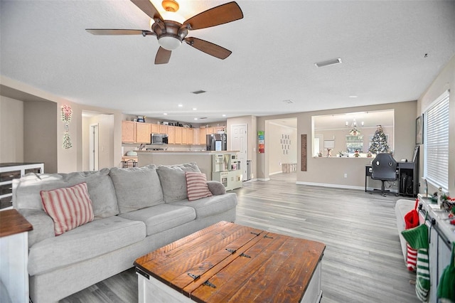 living room featuring ceiling fan with notable chandelier, a textured ceiling, and light hardwood / wood-style flooring