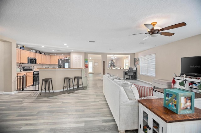 living room featuring a textured ceiling, light wood-type flooring, and ceiling fan